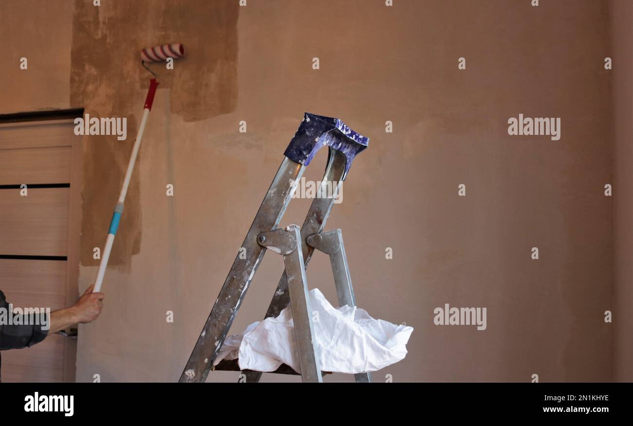 the top of an old aluminum ladder with a white cloth rag on the step against the background of a room wall in the process of priming by a repairman Stock Photo