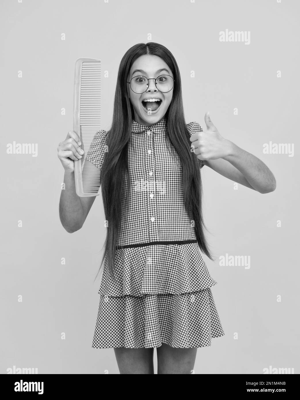 Funny teenager girl brushing hair with comb on yellow isolated studio