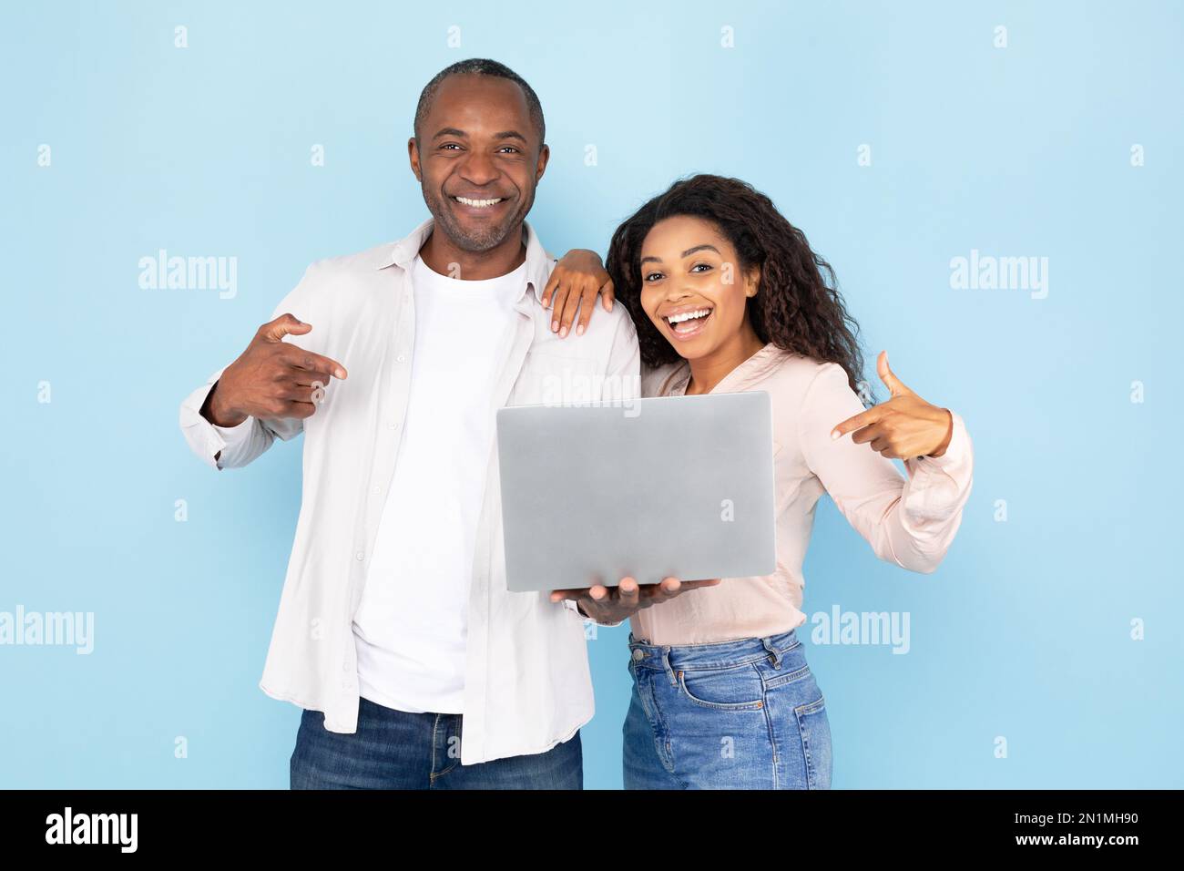 Happy african american couple holding laptop and pointing fingers at ...