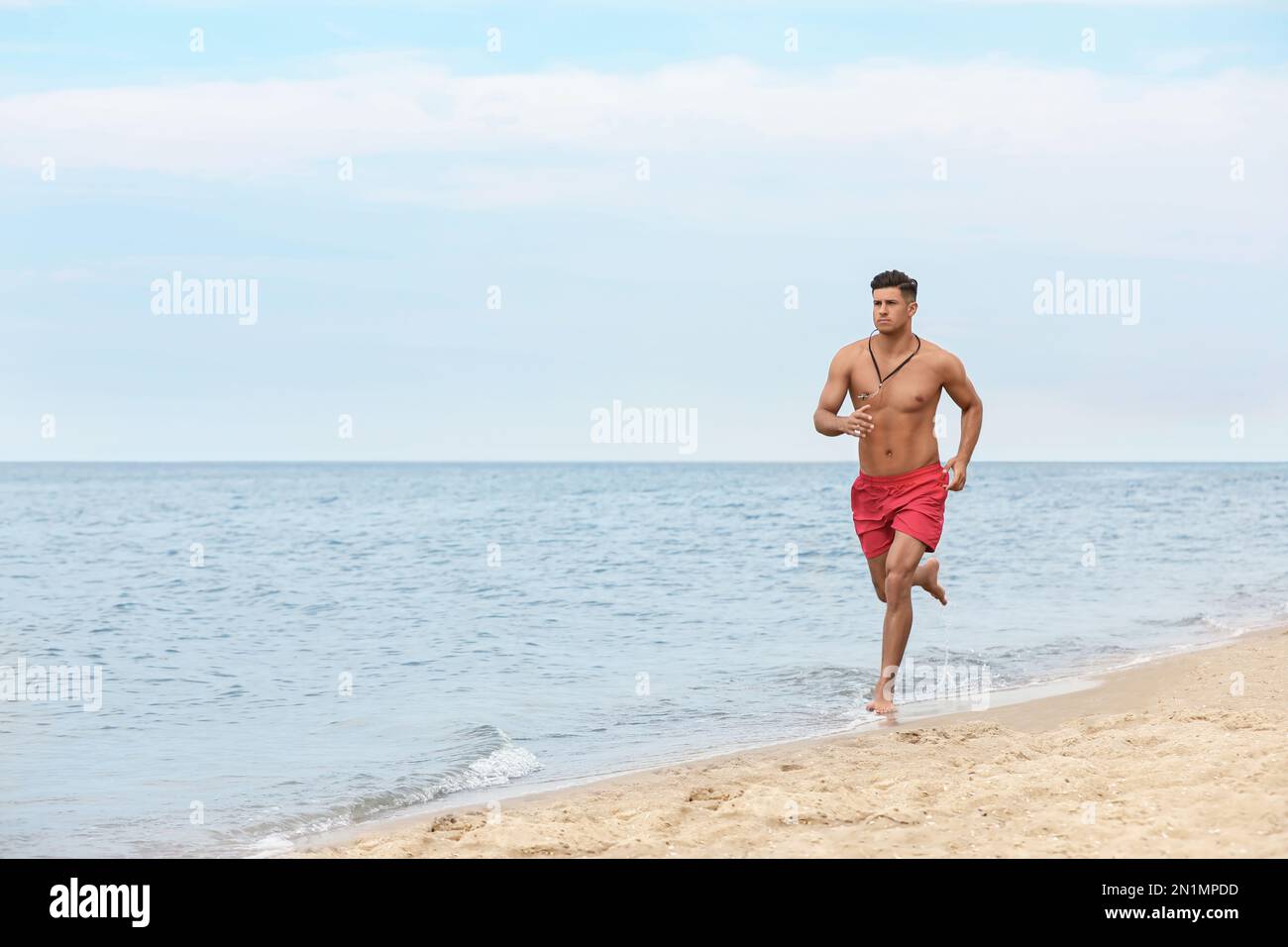Handsome male lifeguard running on sandy beach Stock Photo - Alamy