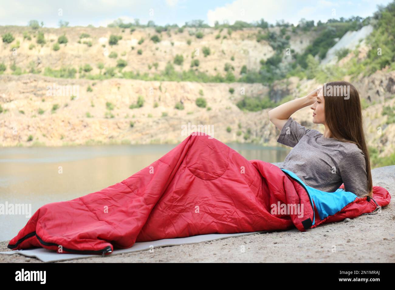 Young camper in sleeping bag on cliff near lake Stock Photo Alamy