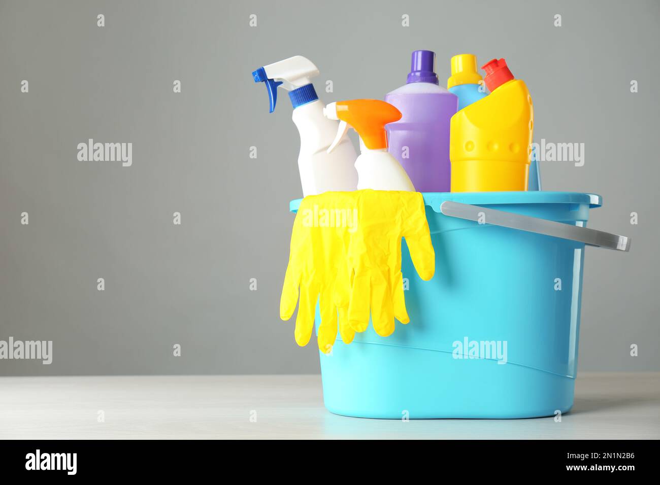 Bucket with cleaning products and gloves on grey table. Space for text ...
