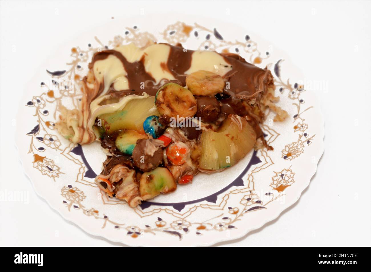 Chocolate mixture with biscuit and different types of chocolate pieces and cream with fresh pineapple ananas and bananas pieces on top on a dough bake Stock Photo