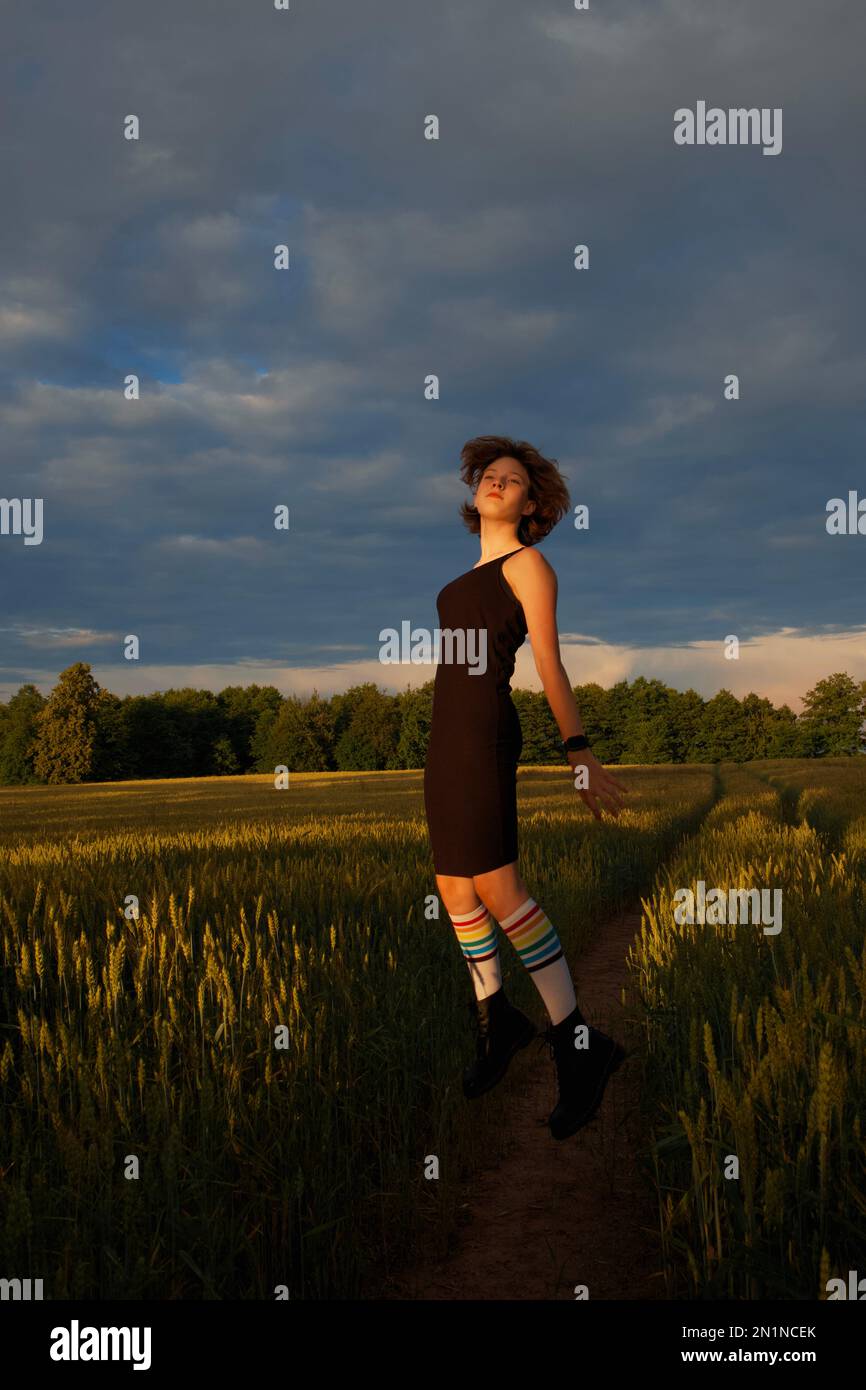A teenage girl wearing knee socks with rainbow stripes jumps high in the air turning her face to the setting sun Stock Photo