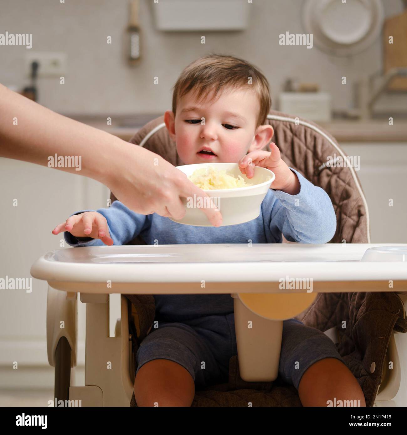 A funny child is eating a grated apple sitting on a kitchen chair