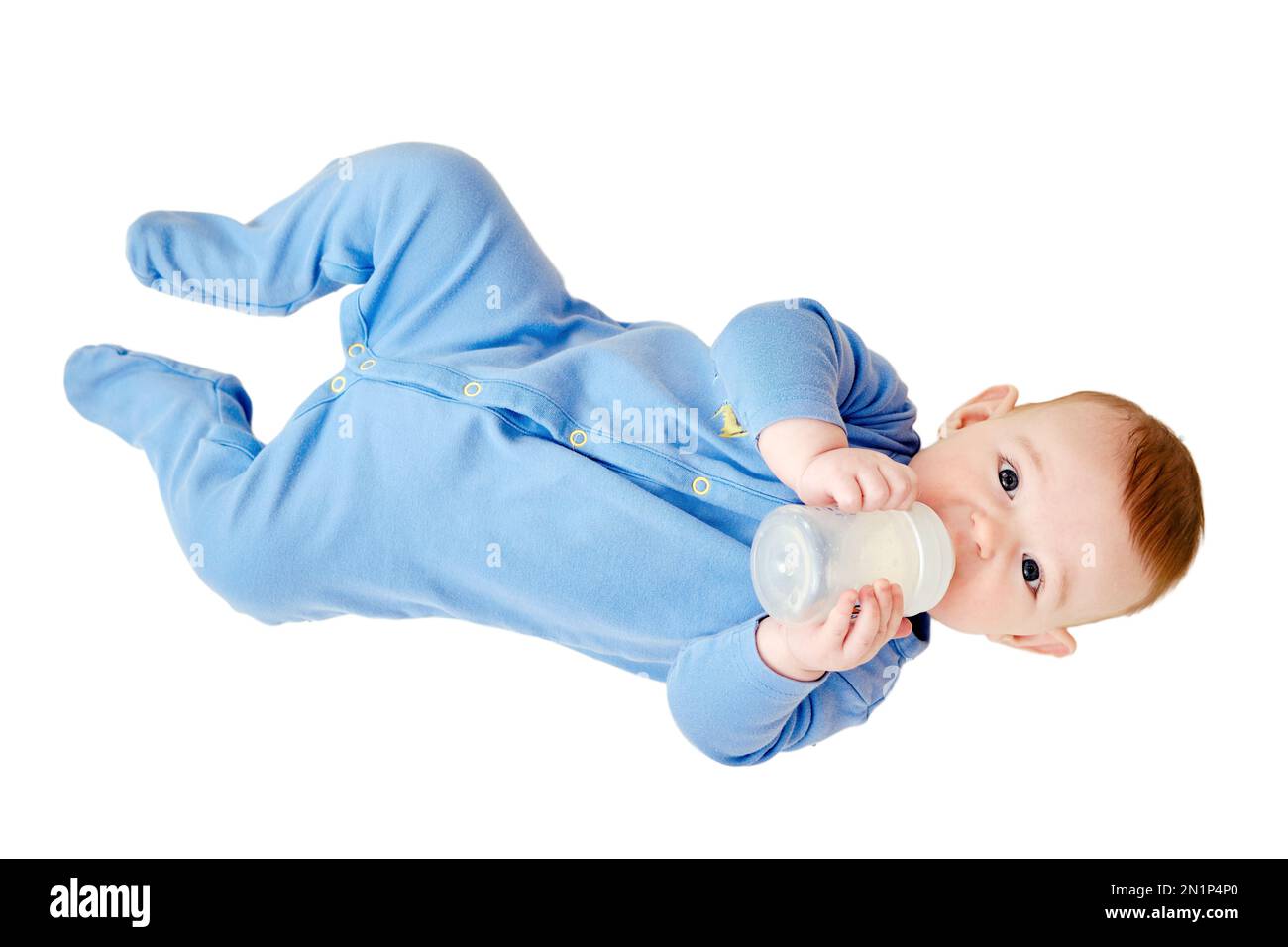 Happy infant baby lies in bed with a bottle of milk in his hands, isolated on a white background