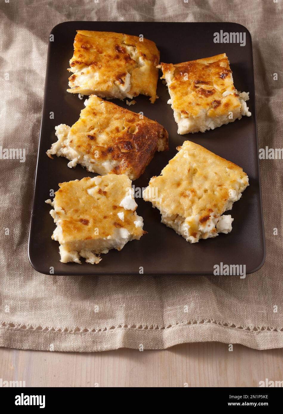 Cheese pie with feta cheese, no crust on a brown plate, beige tea towel, wooden table. Great idea for lunchbox. Stock Photo