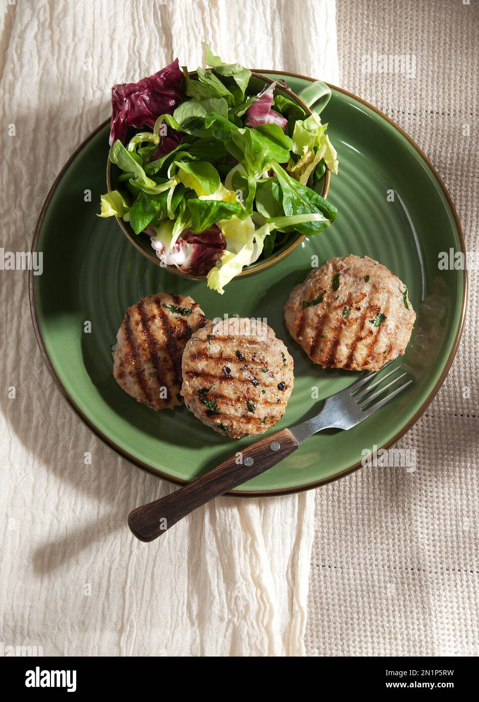 Chicken burgers with green salad on the side. Green plate on light beige, white background. Stock Photo