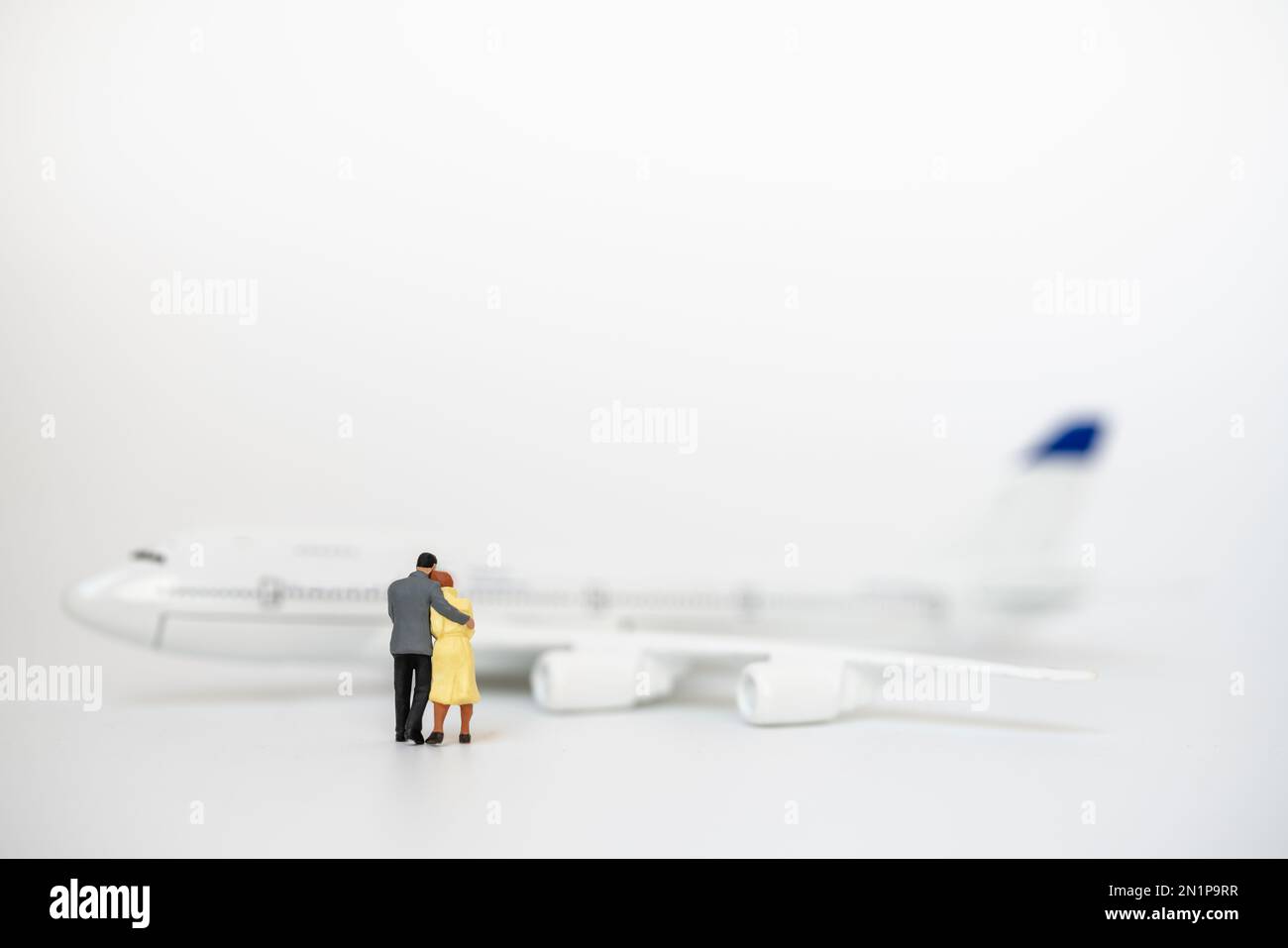 Couple, Family and Travel Concept. Male and female miniature figure people hug and walking to mini airplane model on white background. Stock Photo