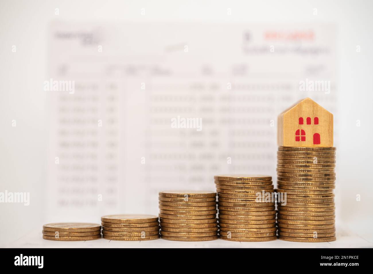Business, Saving and Home Loan Concept. Closeup of wooden house toy on top of stack of gold coins on bank passbook as background. Stock Photo