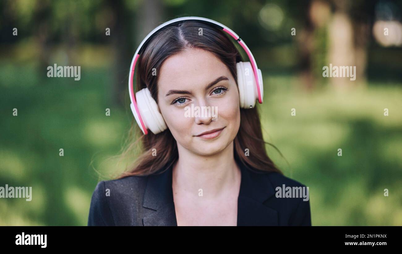 A girl wearing headphones listening to music in a city park. Stock Photo