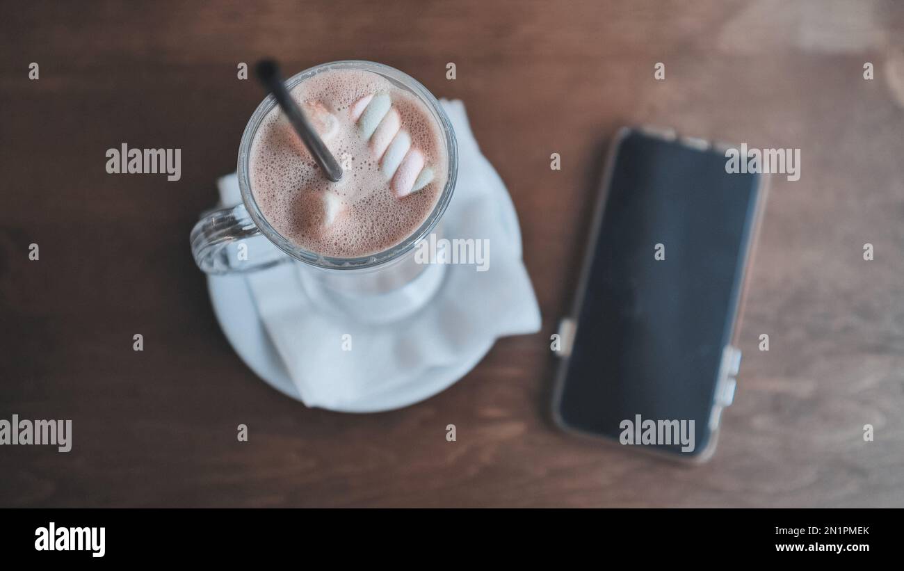A girl drinking a cappuccino in front of her smartphone. Stock Photo