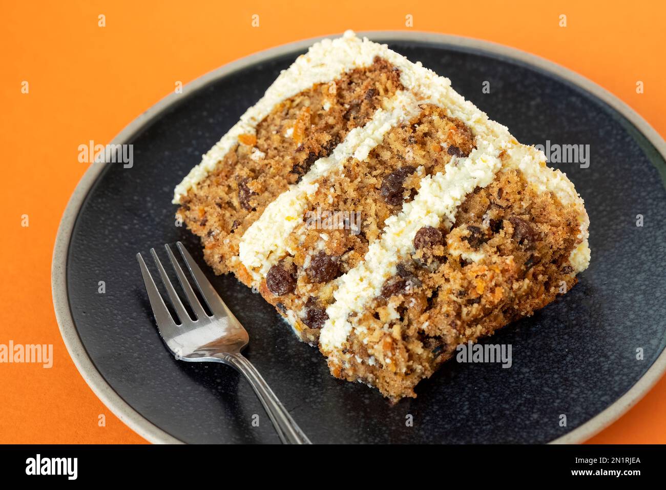 A freshly baked slice of a tiered or layered carrot cake. The cake has three layers with a cream cheese buttercream filling and is served plated Stock Photo
