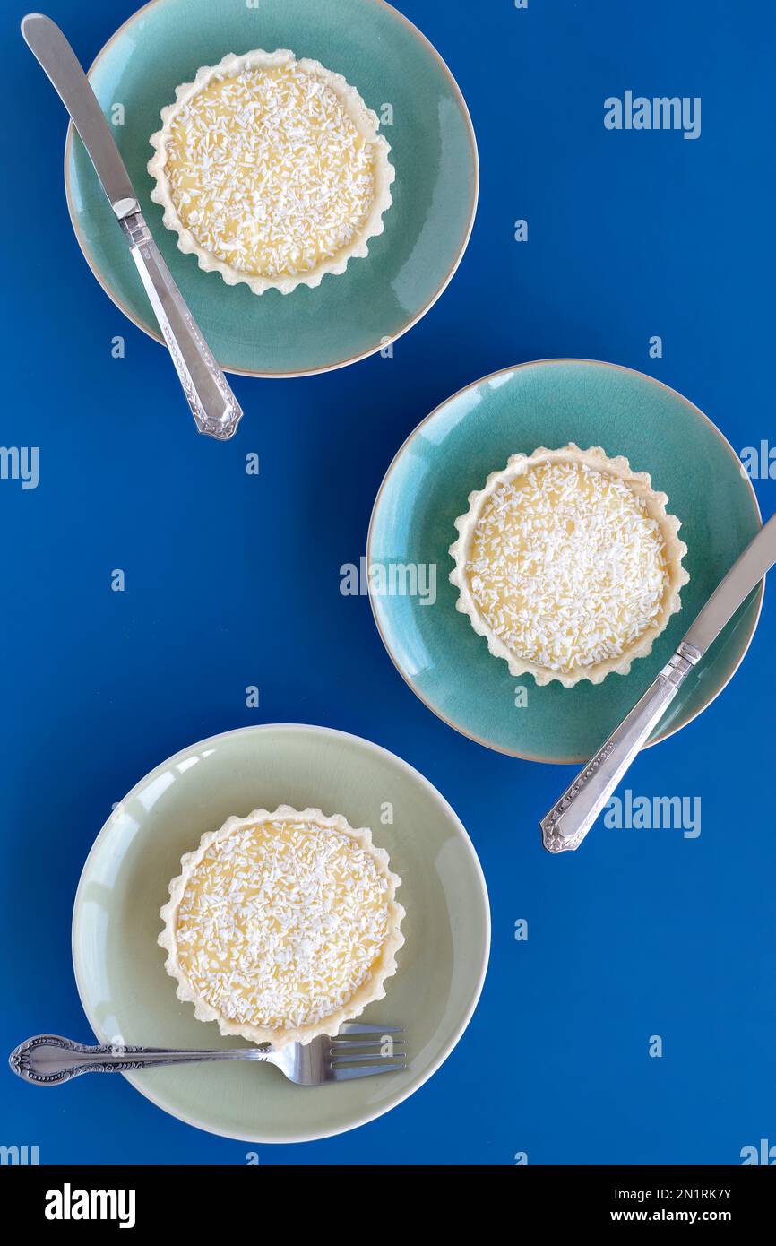 Three home baked tangy lemon tartlets on individual plates. The tartlets are made with a fresh lemon filling in a short crust pastry case Stock Photo