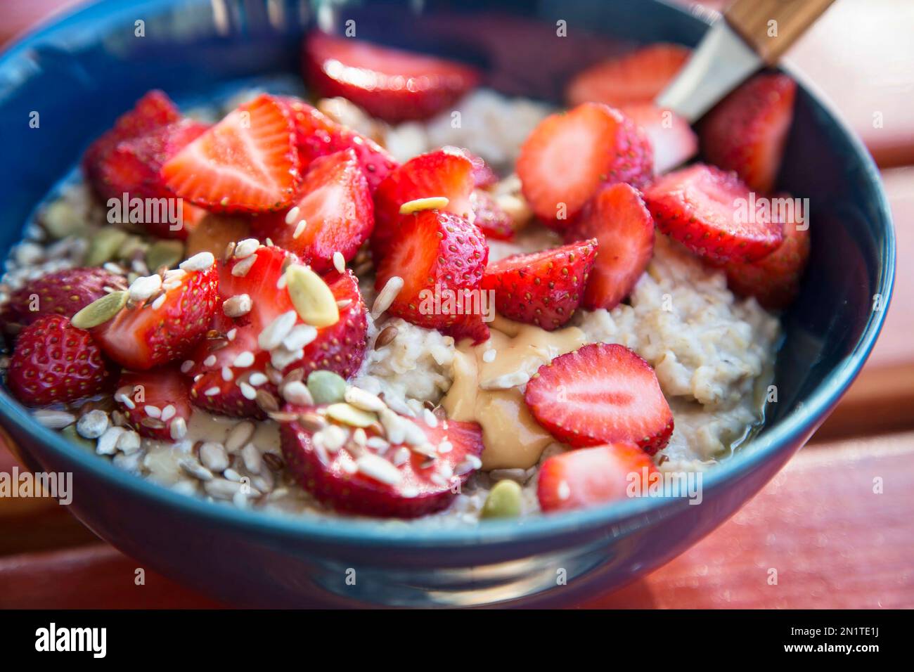 Closeup of fresh porridge bowl with peanut butter, strawberries and nuts Stock Photo