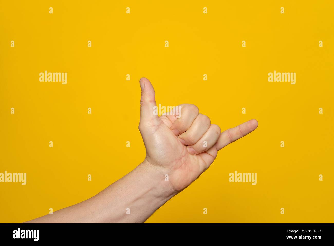 Middle age caucasian man hand over isolated yellow background gesturing hawaiian shaka greeting gesture, phone and communication symbol. Stock Photo