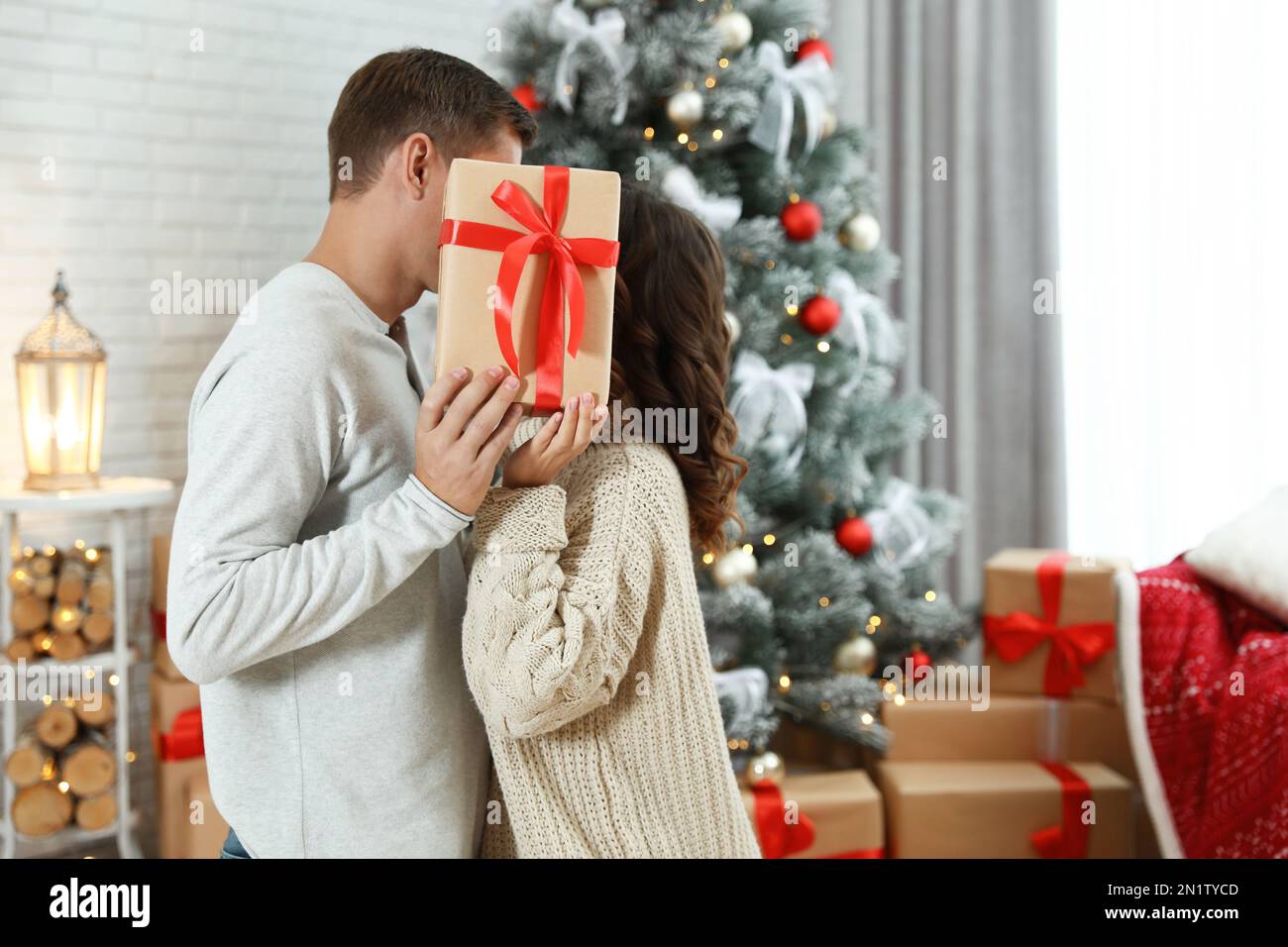 Couple kissing while hiding behind Christmas gift at home Stock Photo Alamy