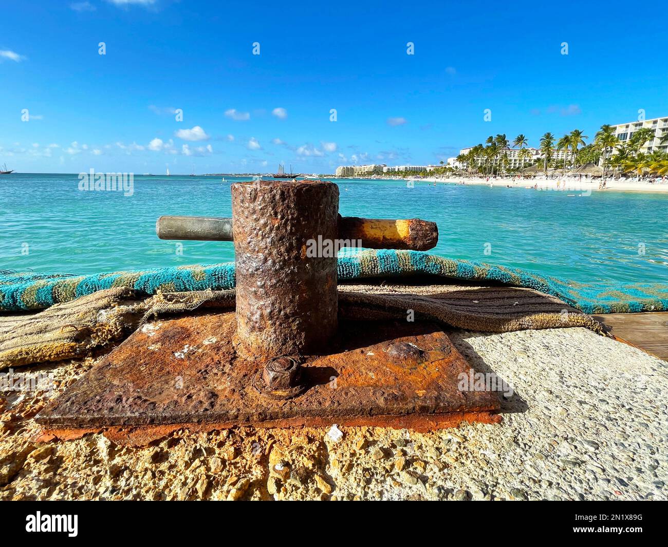 Close up of an old, rusted bitt bollard on a pier in Aruba. Tha Caribbean sea and Palm Beach in the background. Stock Photo