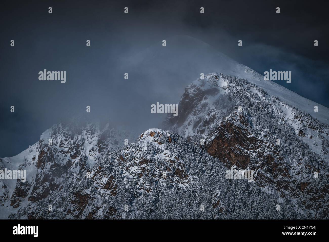 Snowy mountains in a mysterious environment. Fog and black storm clouds cover the mountaintops. Winter landscape, wintertime, snowfall and bad weather Stock Photo