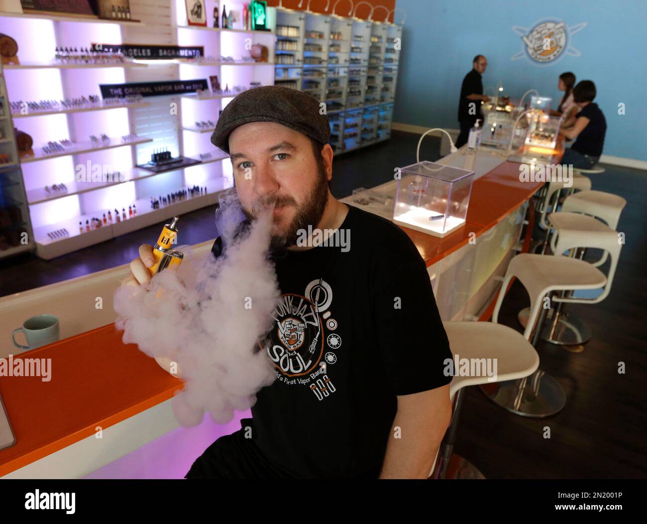 In this photo taken Thursday, July 16, 2015, John "JJ' Jenkins, owner of  the Vapor Spot exhales vapor from an e-cigarette while posing at his store  in Sacramento, Calif. As e-cigarettes rise