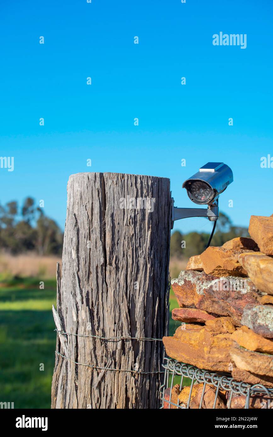 A surveillance security camera attached to a wooden gate post on a farm