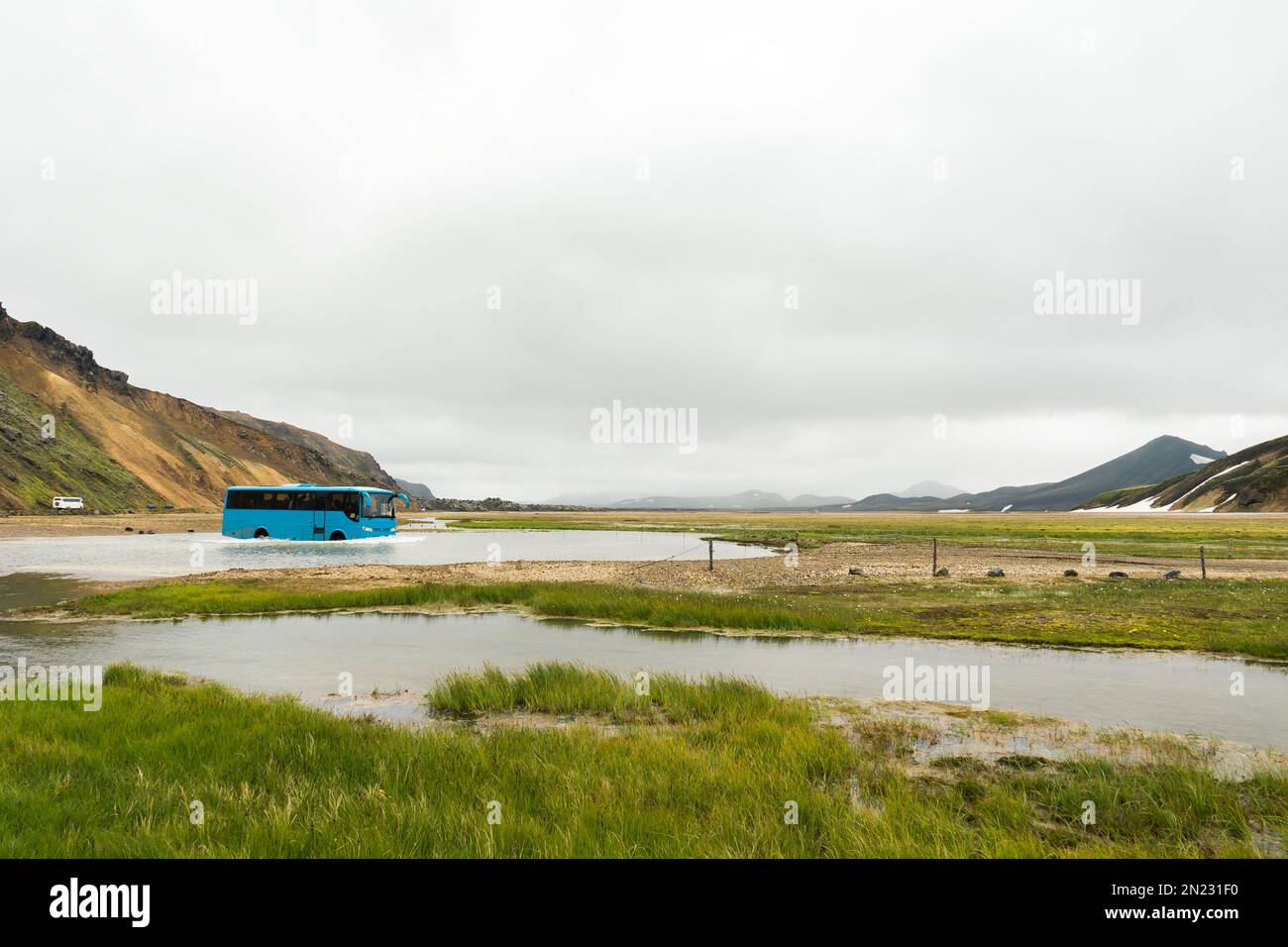 Bus crossing a river with hikers and adventurers in Landmannalaugar on a cloudy day Stock Photo