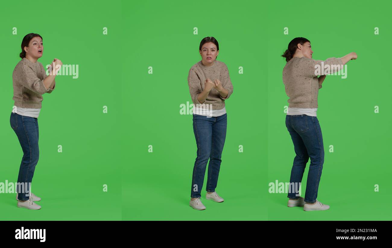 Aggressive woman clenching fists and being violent in studio, acting furious in conflict and having argument. Girl preparing to fight, acting negative over full body greenscreen backdrop. Stock Photo