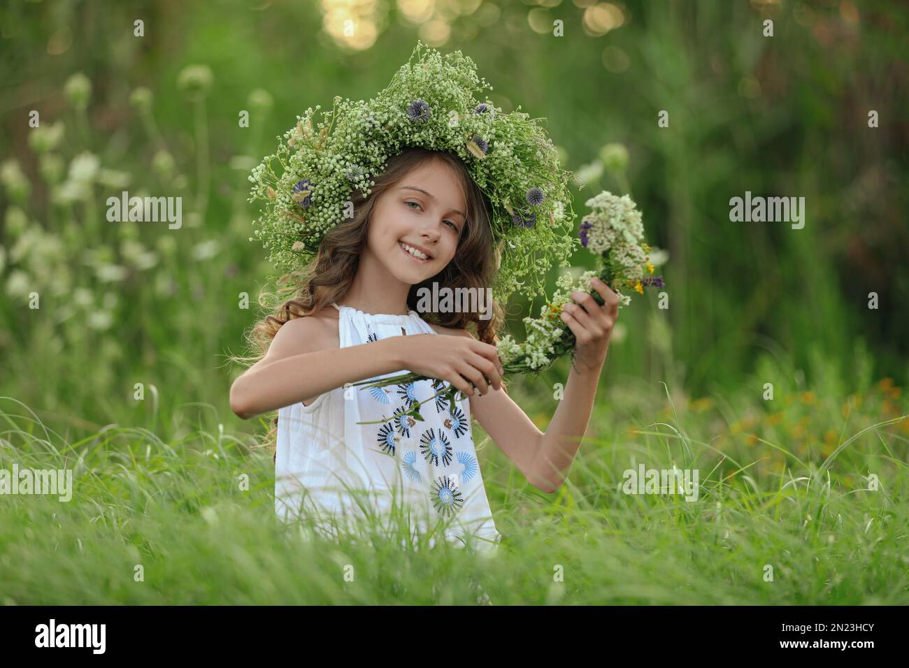 Cute little girl wearing wreath made of beautiful flowers in field ...