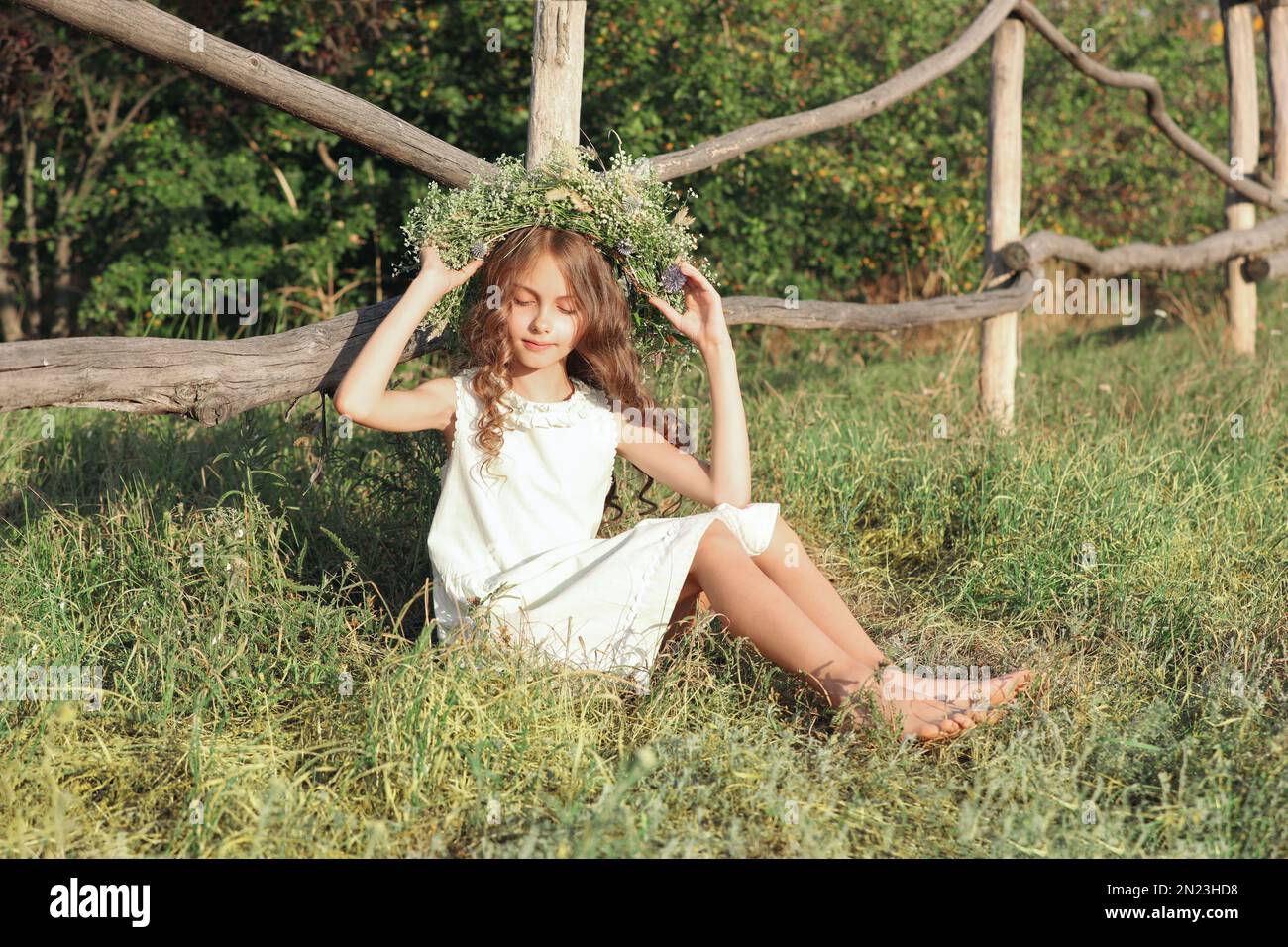 Cute little girl wearing wreath made of beautiful flowers near wooden ...