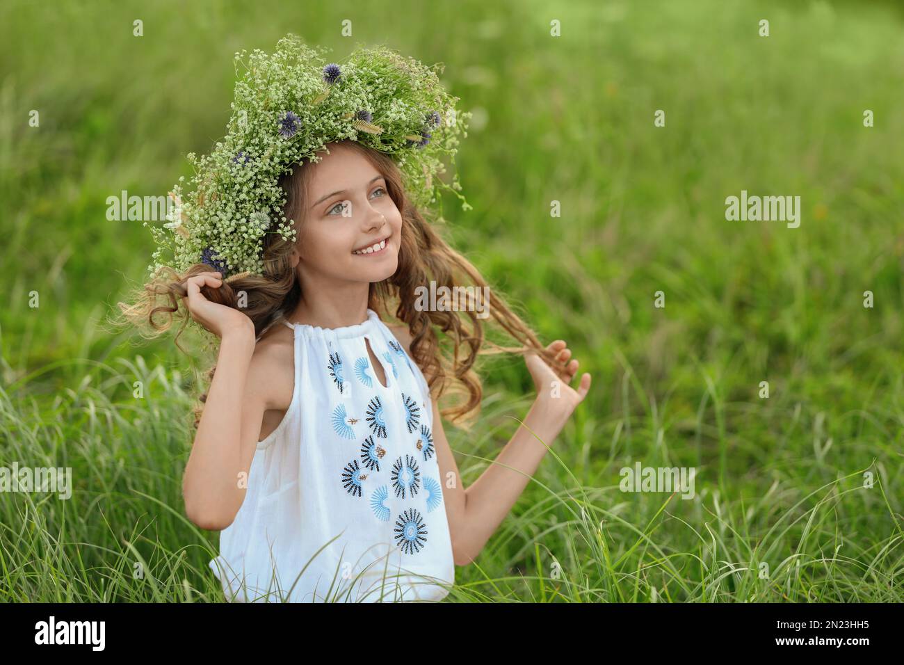 Cute little girl wearing wreath made of beautiful flowers in field ...