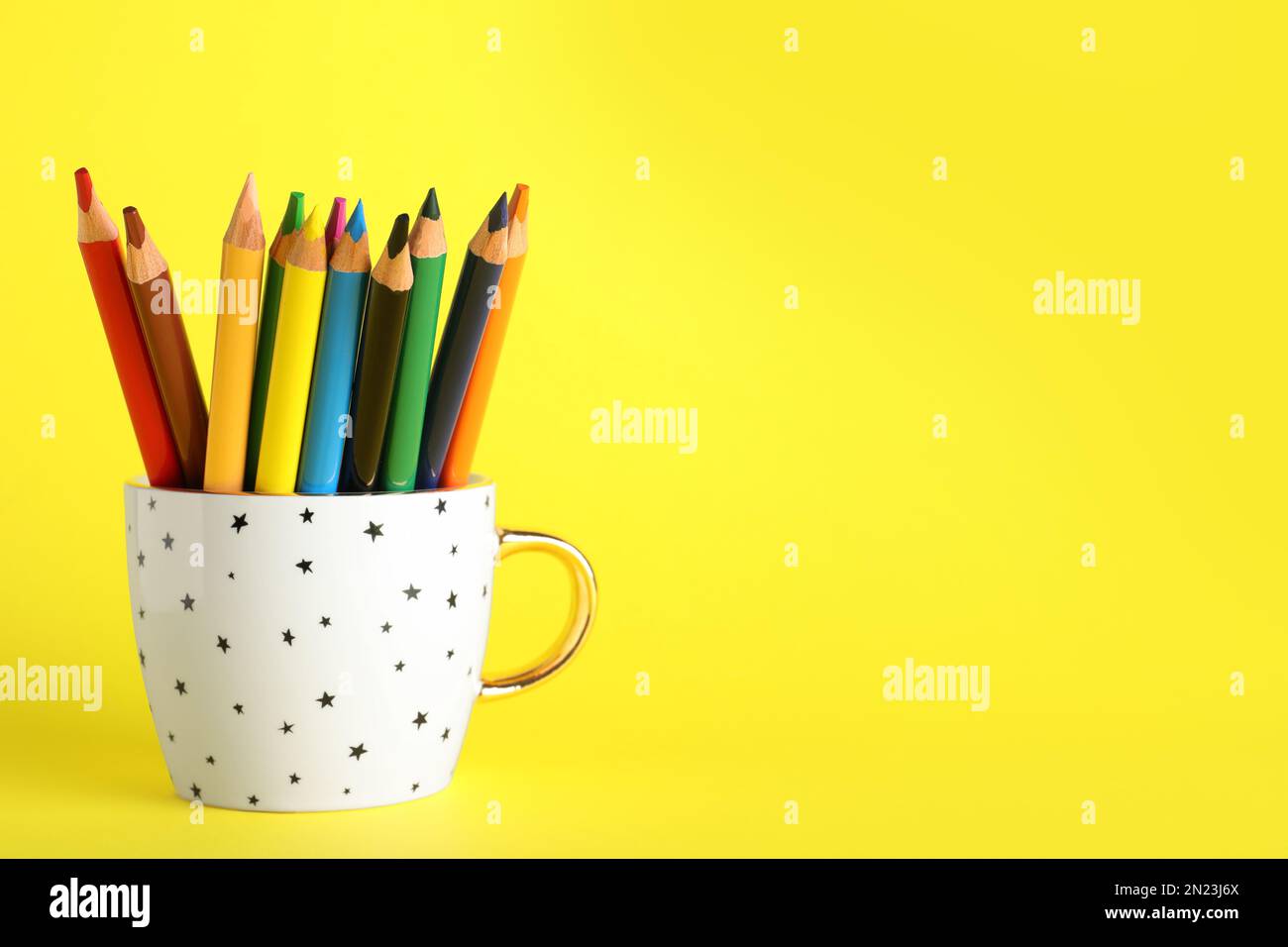 Colorful pencils in cup on yellow background. Space for text Stock Photo