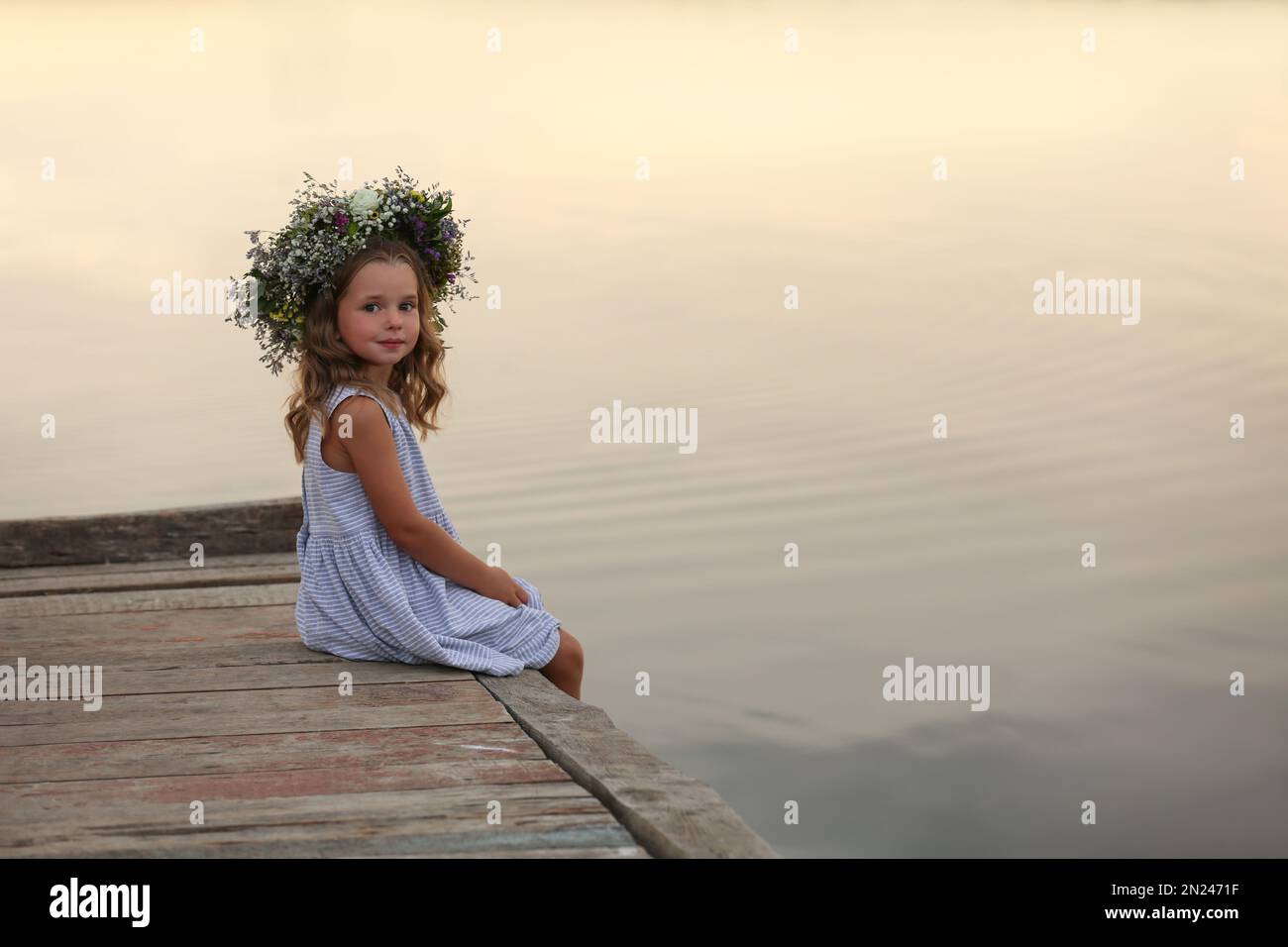 Cute little girl wearing wreath made of beautiful flowers on pier near ...