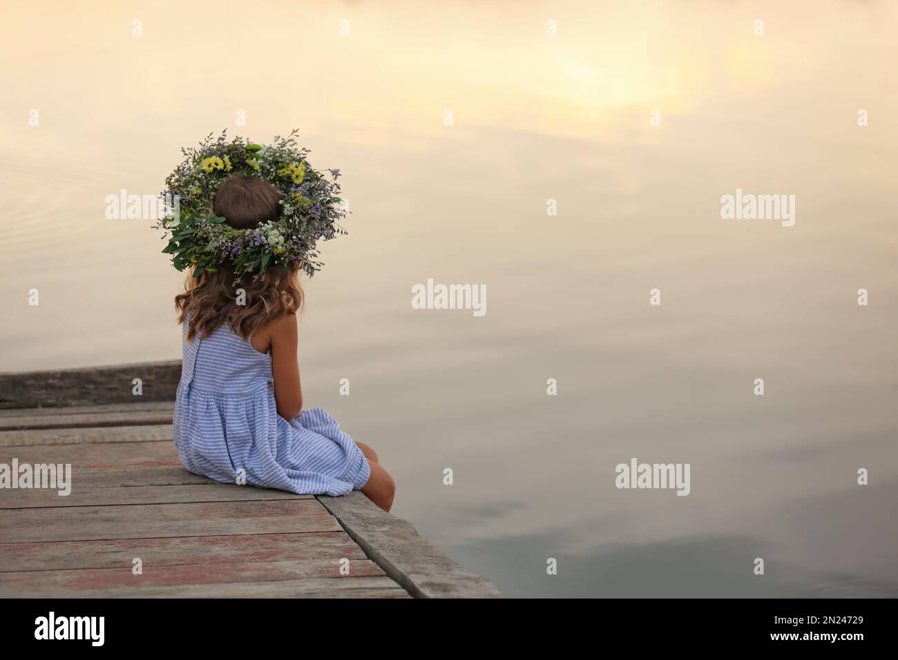 Cute little girl wearing wreath made of beautiful flowers on pier near ...