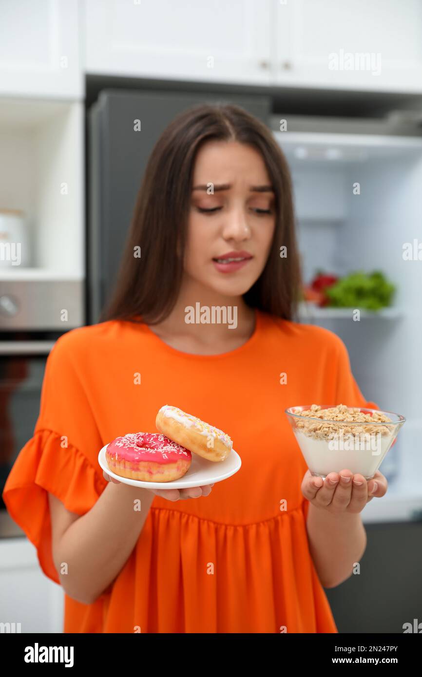 Woman choosing between healthy breakfast and doughnuts in kitchen ...