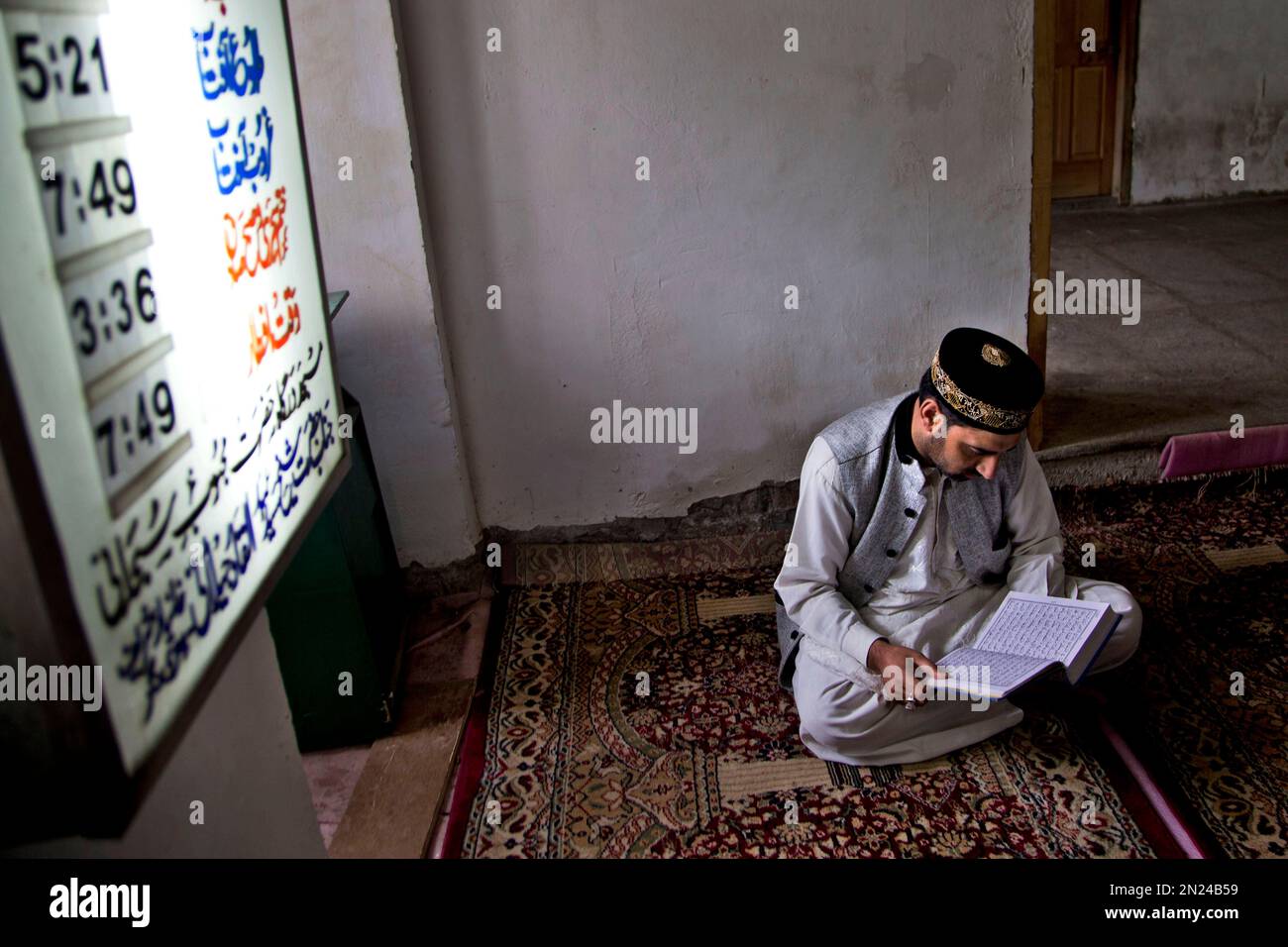A Kashmiri Muslim man recites holy Quran inside a mosque as signboard ...