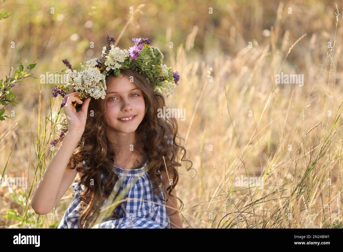 Cute little girl wearing wreath made of beautiful flowers in field on ...