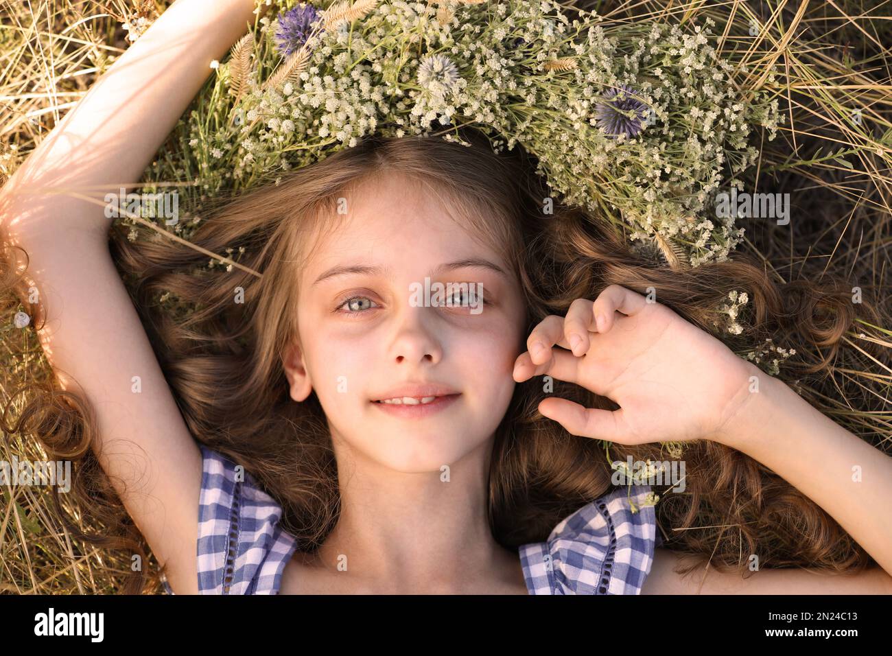 Cute little girl wearing wreath made of beautiful flowers on green ...