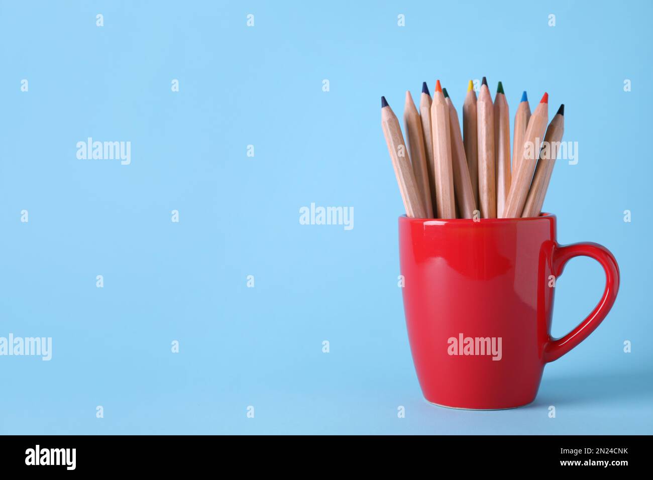 Colorful pencils in cup on light blue background. Space for text Stock Photo