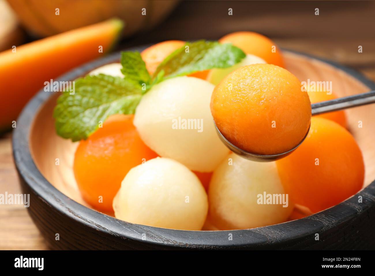 Scoop with melon ball near plate of fruit salad, closeup Stock Photo