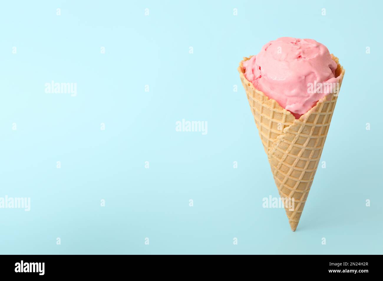 Delicious pink ice cream in waffle cone on light blue background. Space ...