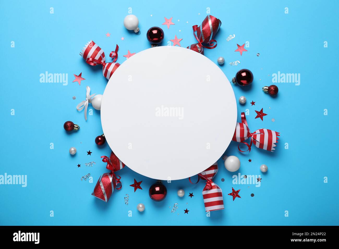 Flat lay composition of Christmas crackers, decorations, shiny confetti and blank paper on light blue background. Space for text Stock Photo