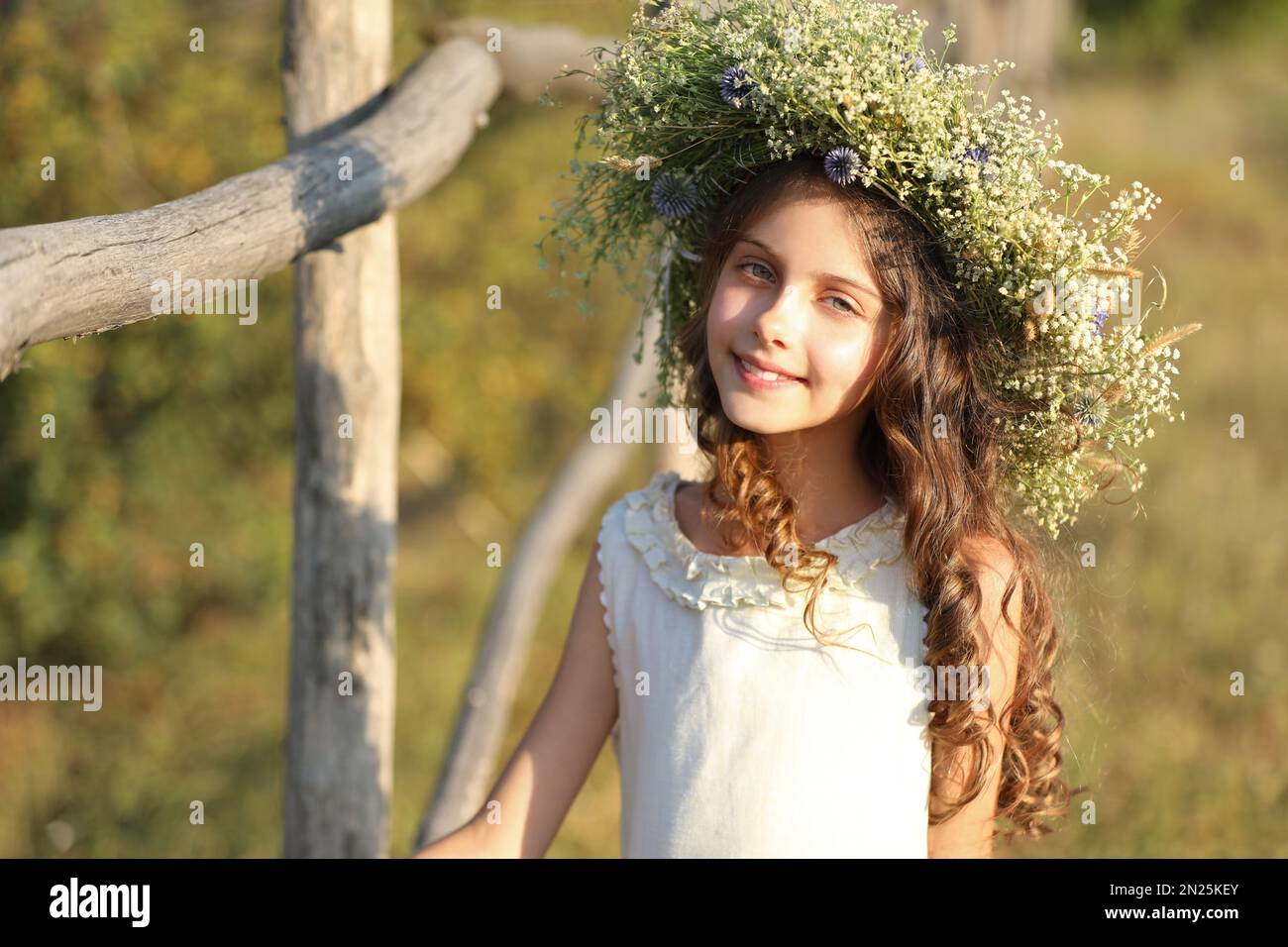 Cute little girl wearing wreath made of beautiful flowers near wooden ...