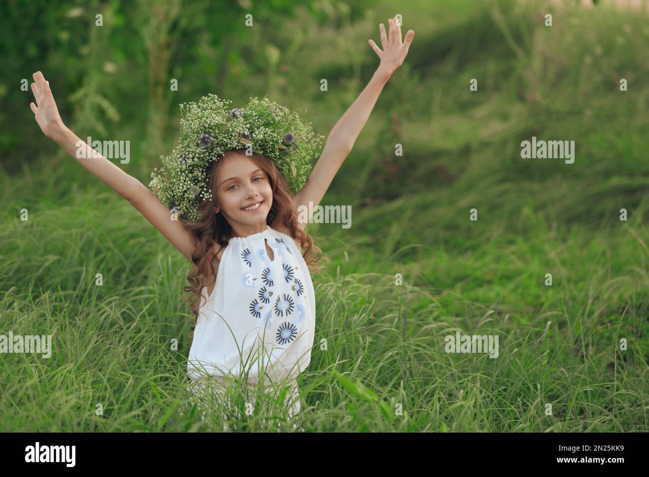 Cute little girl wearing wreath made of beautiful flowers in field ...