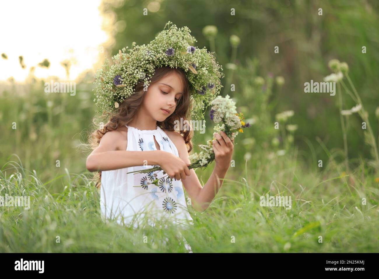 Cute little girl wearing wreath made of beautiful flowers in field ...