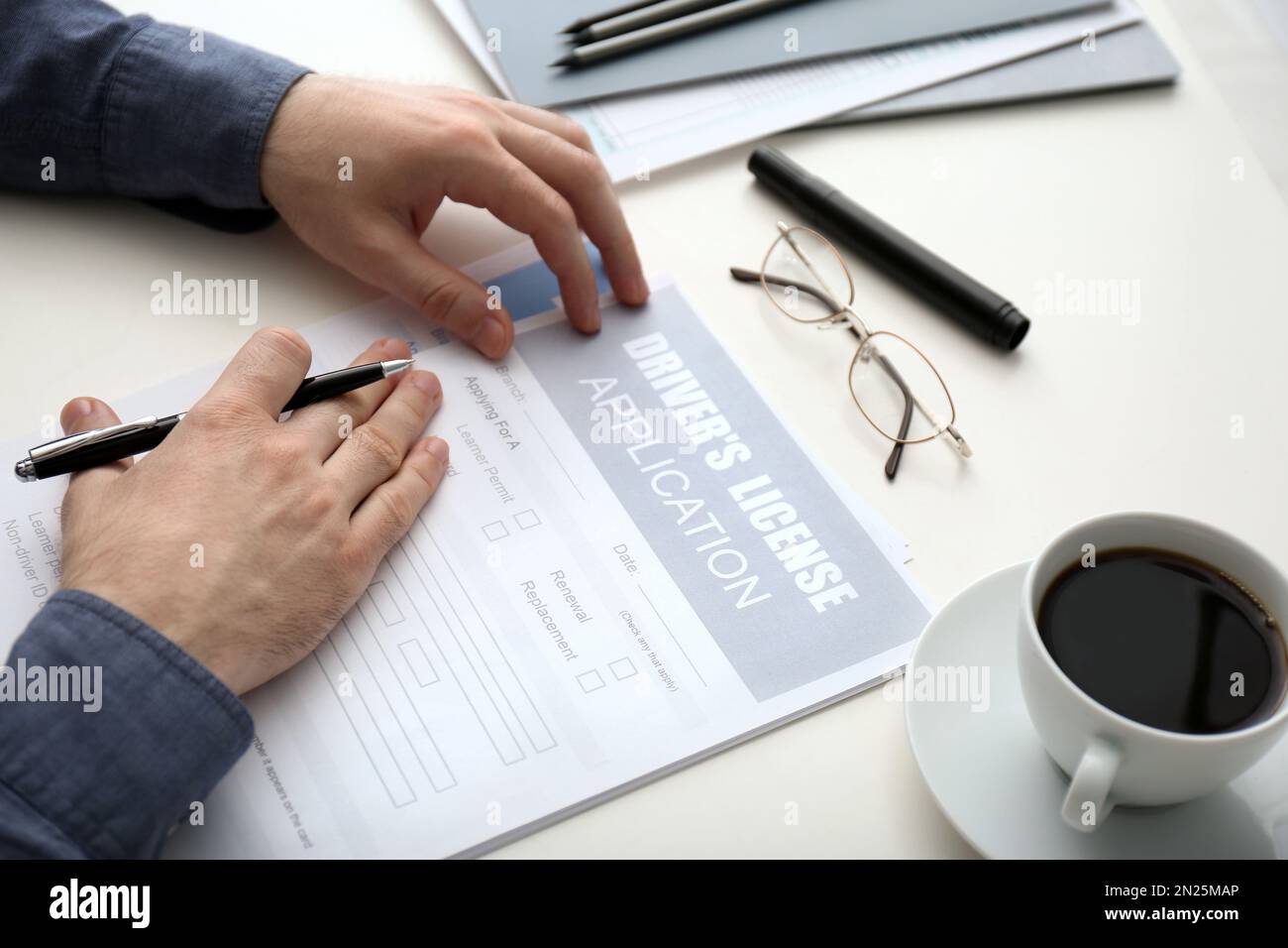 Man filling in driver's license application form at white table ...