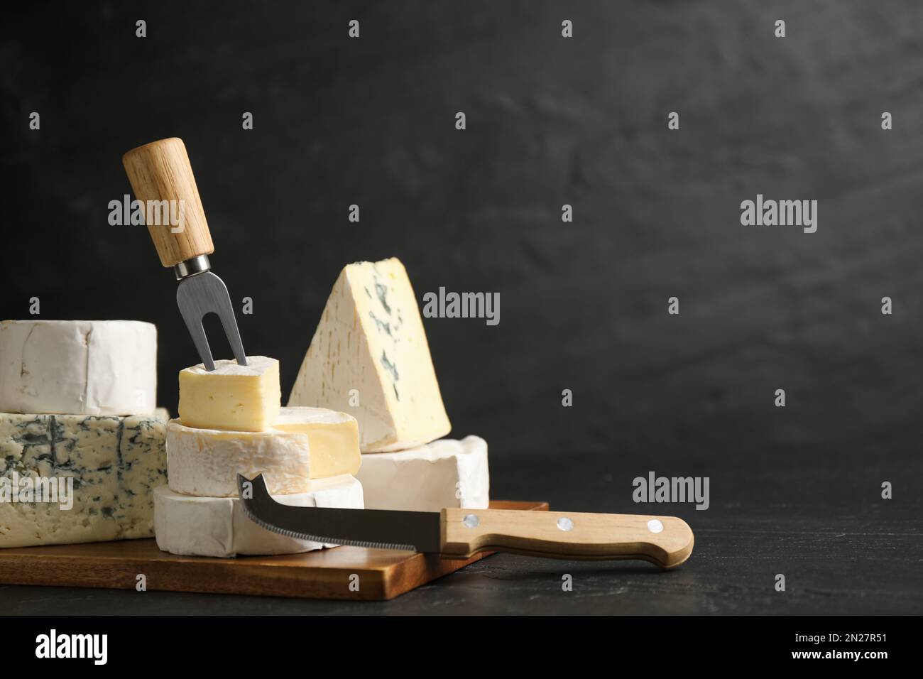 Different types of cheese, knife and fork on black table. Space for