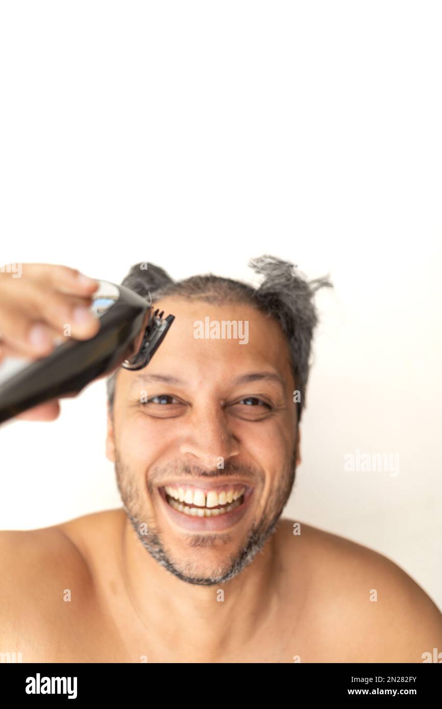 Handsome gray-haired man is cutting hair himself with an electric hair clipper. Stock Photo