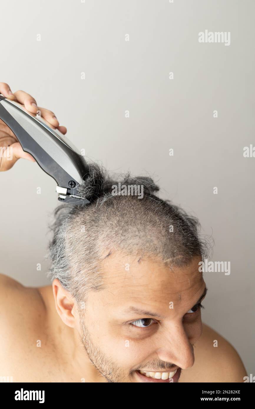 Handsome gray-haired man is cutting hair himself with an electric hair clipper. Stock Photo
