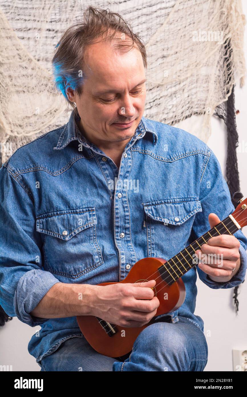 Man in blue denim jacket playing small ukulele Stock Photo