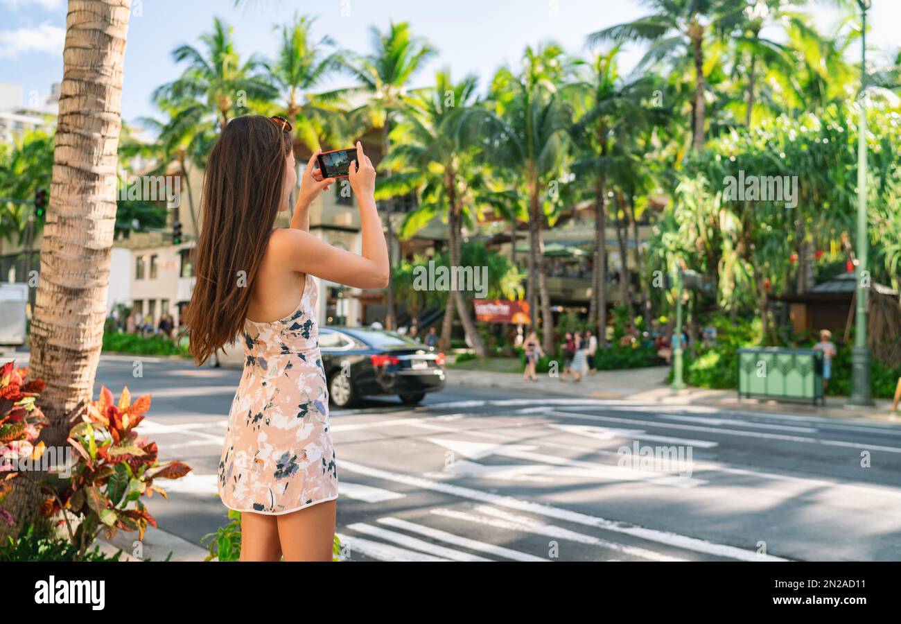 Honolulu city woman tourist taking pictures with phone camera walking